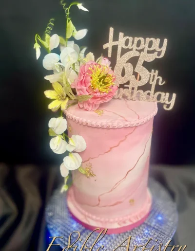Elegant pink birthday cake with floral accents and 65th birthday topper
