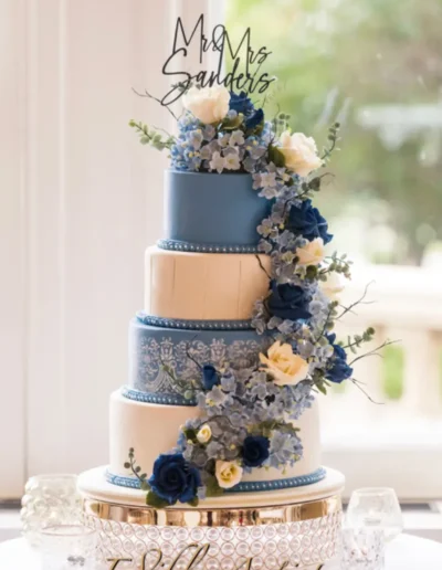 Elegant tiered wedding cake with blue floral accents and custom topper