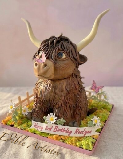 Highland cow sculpted birthday cake with realistic edible details and floral accents